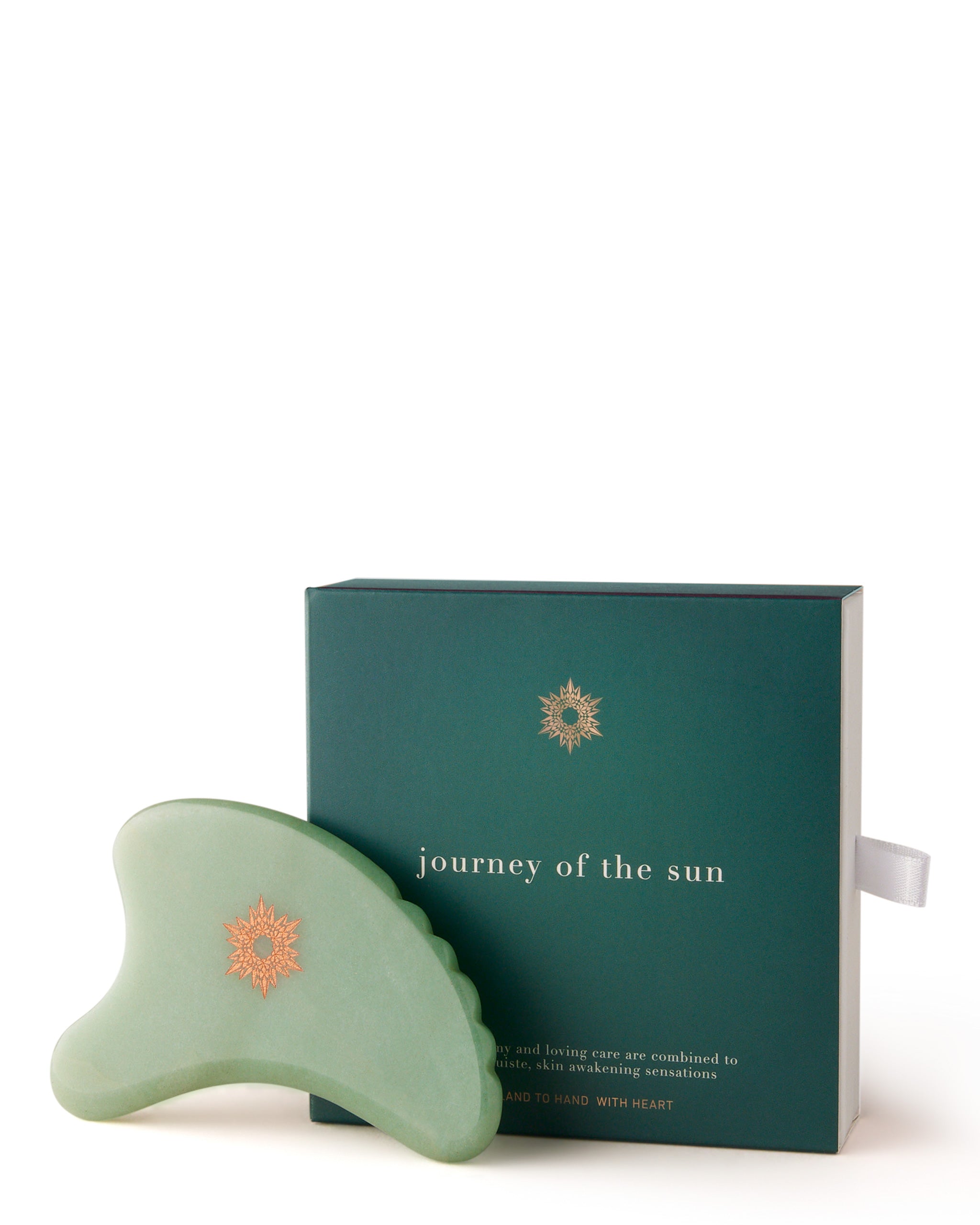 A green Gua Sha tool next to its packaged box with the text 'Journey of the Sun' and a white string attached.
